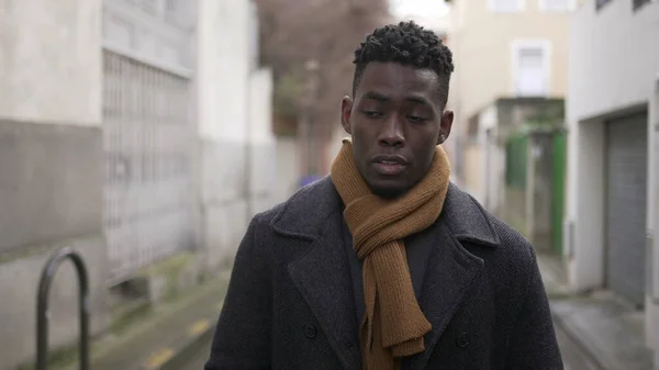 Sad upset black African man walking outside in city with moody depressed emotion