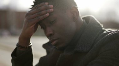 Worried black man suffering alone in emotional pain outside in city sidewalk street