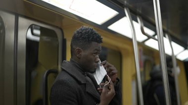 Metroyla gidip gelirken, siyah Afrikalı genç bir adam covid-19 yüz maskesi takıyor.