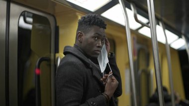 Metroyla gidip gelirken, siyah Afrikalı genç bir adam covid-19 yüz maskesi takıyor.