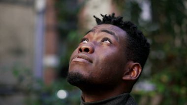 Genç siyahi Afrikalı adam gökyüzüne bakıyor umutla ve inançla