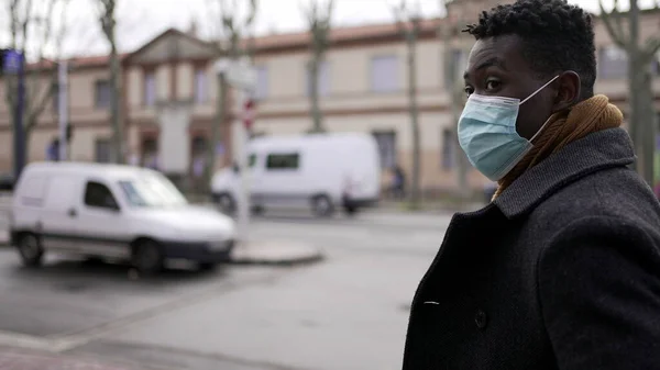 Young black man wearing covid-19 face mask walking in city downtown during pandemic, tracking shot