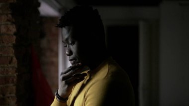 Pencere kenarında durup hayatı düşünen Afrikalı bir adam. Endişeli duygular