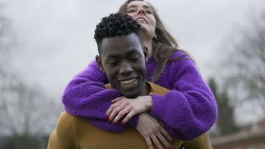 Sevgilisini sırtında taşıyan bir erkek arkadaş. Genç milenyum ırklar arası çift, kız erkeğe sırt sırta