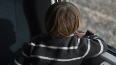 Hızlı trenle seyahat eden mutlu bir çocuk pencereden dışarı bakıyor. Ağır çekimde, hızlı trendeki küçük çocuğun arkası.