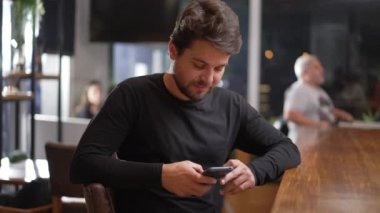Elinde telefonla kahve dükkanında oturan genç bir adam. İnternette akıllı telefondan arama yapan kişi. Cep telefonu ekranına bakan adam.