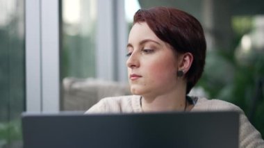 Laptopun önünde kahve dükkanının penceresinden dışarı bakan dalgın genç bir kadın. Düşünceli kızıl saçlı kız düşüncelere dalmış. İş çözümünü düşünen kişi