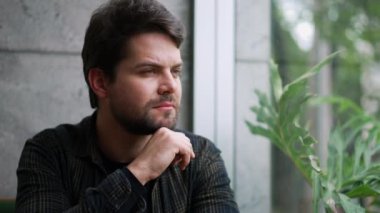 Pencereden dışarı bakan genç adam profili. Yüzü yakın plan. Düşünceli ciddi ifade.