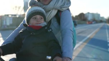 Anne önünde oturan çocukla bisiklete biniyor. Soğuk kış günü ebeveynler şehirde bisiklet sürüyor.