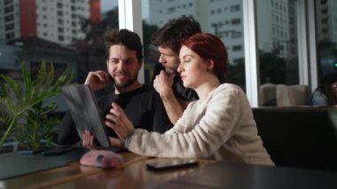 İnsanlar kafeteryada tablet tutan online içeriği tartışıyor. Modern teknolojik aygıt kullanan üç bin yıllık bir grup.