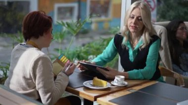 İş kadını müdürü kahve dükkanında oturan kadın çalışanlara tablet gösteriyor. Bayan Girişimci yeni çalışana işi açıklıyor. Kadın notlar yazıyor öğrenme talimatları