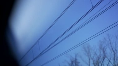 Mavi gökyüzünde geçen elektrik teli direklerini gören tren penceresinin POV 'u.