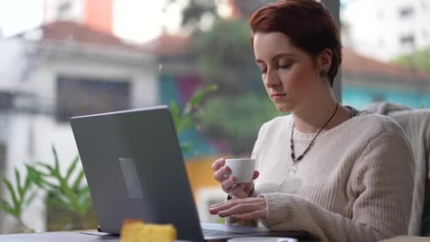 1人の若い女性がカフェの場所に座って熟考してラップトップコンピュータの前でコーヒーを選んでいます オンラインでコンテンツを読む人 — ストック動画
