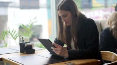 Tablete bakan bir kadın kafeteryada oturuyor. Modern teknoloji aygıt ekranı kullanılarak internete erişilen kişi