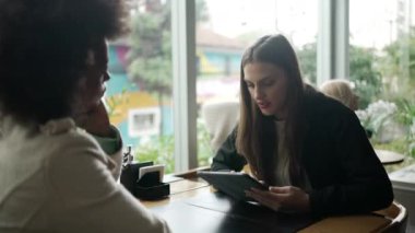 Genç bir kadın arkadaşlarıyla kafede otururken tablet kullanıyor. Kafe restoranında internet ya da sosyal medyada modern teknolojiyi kullanan insanlar