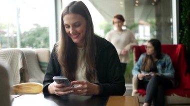 Kahve dükkanında telefondaki mesaja gülümseyen mutlu kadın. Kafe restoranında elinde akıllı telefon tutan bir kız.