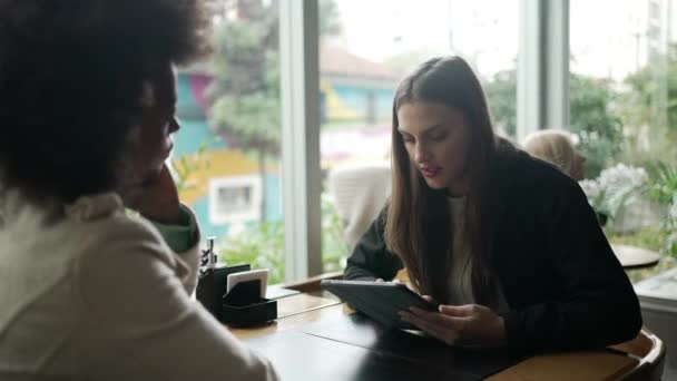 友人とコーヒーショップに座っているタブレットを使用して若い女性 インターネットやソーシャルメディアを閲覧するカフェレストランで現代技術を利用する人々 — ストック動画