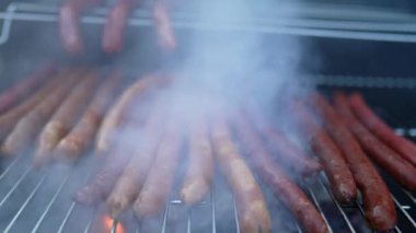 Barbekü sosisleri ızgarada, alevler içinde ağır çekimde sosisli pişiriyor.