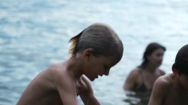 Yaz tatilleri sırasında gölün kenarında duran ıslak çocuk. Sarışın erkek çocuk profili doğada duruyor. Samimi ve otantik