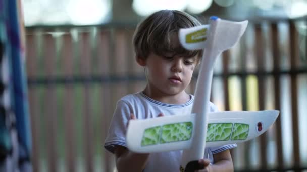 一个可爱的小男孩抱着巨大的抛掷泡沫平面 在公寓楼露台为小朋友们提供的飞行玩具 — 图库视频影像