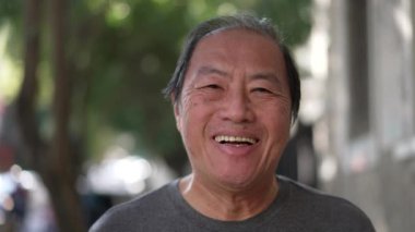 Mutlu Asyalı adam portresi. Yakından şehrin kaldırımındaki kameraya doğru yürüyor..