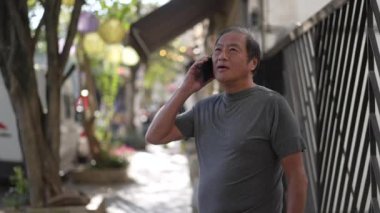 Üst düzey bir Asyalı telefonda sokak kaldırımında dikiliyor. Şehirde akıllı telefondan konuşan sıradan bir yaşlı.