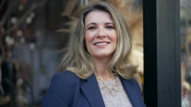 Yerel iş yerinin önünde kameraya gülümseyen orta yaşlı bir kadının portresi. Gülümseyen kişinin yakın yüzü