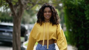 Kendine güvenen siyah bir kız öne doğru yürür. Genç ve mutlu bir Afro-Amerikan kadın şehir kaldırımında kameraya doğru yürüyor..