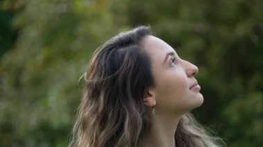 Düşünceli genç bir kadın dışarıda dikilip gökyüzüne yakından bakıyor. Sessizce meditasyon yapan biri.