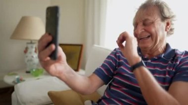 Mutlu kıdemli adam akıllı telefon kullanarak ailesine el sallıyor. Gülüyor ve gülümsüyor.