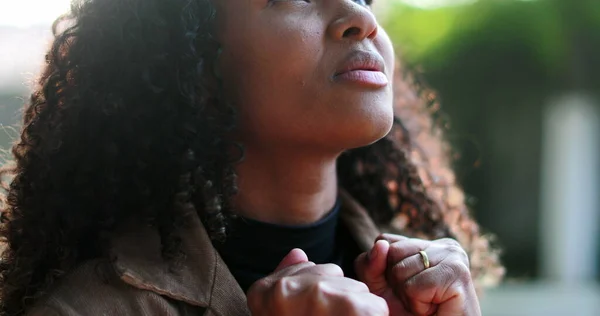 African woman praying to God outside seeking faith and HOPE outside in sunlight