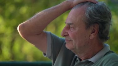 Düşünceli, olgun bir adam, zihinsel bir düşünceyle dışarıda oturan saçlarını düzeltiyor. Park 'taki son sınıf öğrencisinin düşünceli profili.