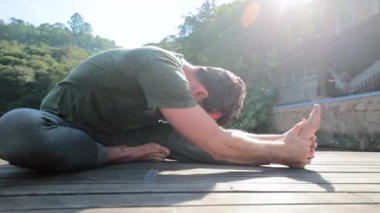 Yogada bacağını ve vücudunu açan bir adam dışarıda poz veriyor.