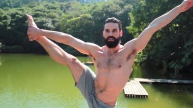 Yakışıklı atletik formda bir adam Yoga eğitirken bir bacağının üzerinde duruyor. Vücudunu esnetiyor ve dengede duruyor.