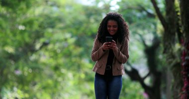 Dışarıda yürürken cep telefonu kullanan Afrikalı bir kadın. Telefon ekranında yürüyen biri.