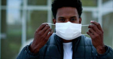 African man putting on covid mask walking forward to camera