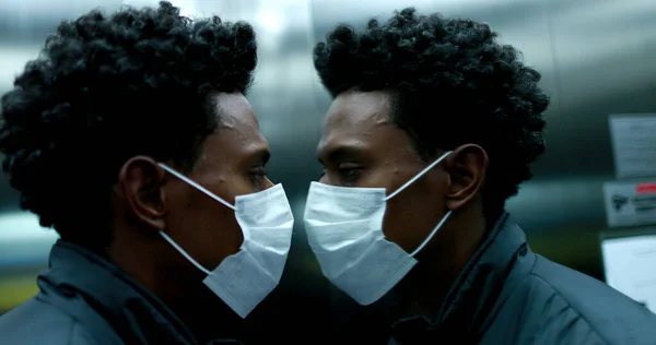 Black african man wearing face mask looking at himself in elevator mirror
