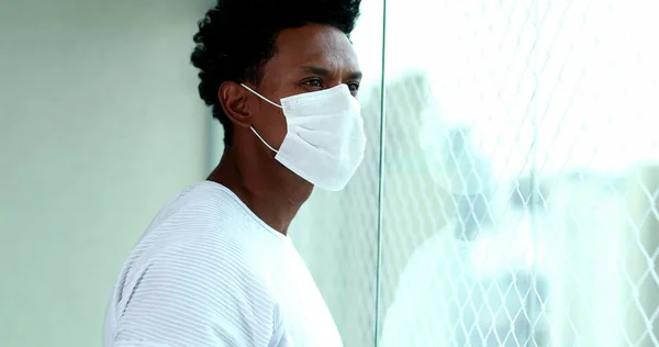 African American Man Wearing Virus Prevention Mask Looking Out Apartment — Stock fotografie
