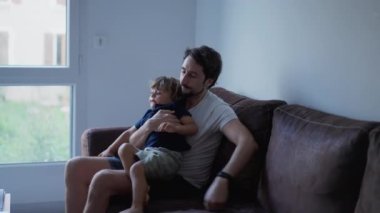 Baba ve oğul evdeki kanepede birlikte takılıyorlar. Baba kucağında samimi bir çocuk. Otantik gerçek aile ilişkisi