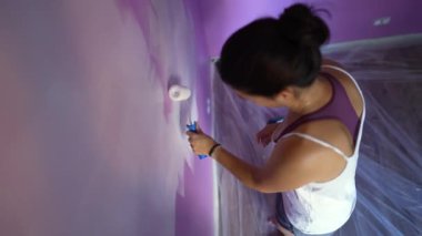 Mor duvarı beyaz renge boyayan kişi. Ev tadilatı yapan kadın yeni bir ev boyuyor. Kadın ressam.