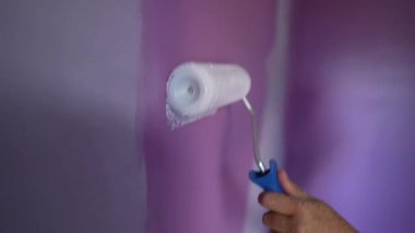 Mor duvara beyaz renk uygulayan yakın plan boya silindiri. Ev onarımı yapan kişi