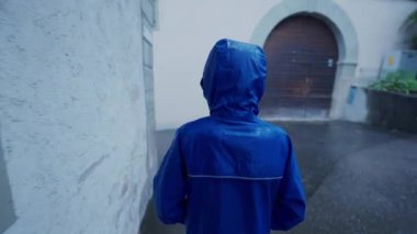 Yağmurlu günlerde sokakta yürürken yağmurluk giyen bir çocuk. Çocuk mavi su geçirmez ceket giyiyor.