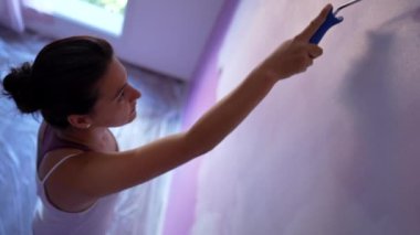 Duvarı boyayan kadın, evini yeniliyor. Kadın ressam boya silindirini hareket ettiriyor. Ev işi numarası.