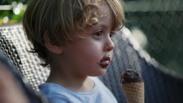 外でチョコレートアイスクリームコーンを食べている1人の熟考的な少年 子供はデザートを食べる — ストック動画