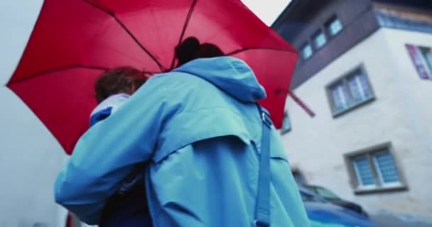 雨天在红色雨伞下散步的人 下午下雨时抱着孩子的母亲的背 — 图库视频影像