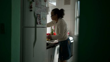 Güney Amerikalı son sınıf öğrencisi, mutfak lavabosunda duruyor. Yaşlı bir İspanyol kadın bulaşık yıkıyor.