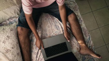 Yatakta dizüstü bilgisayar kullanan genç Brezilyalı bir adam. Güney Amerikalı Latin kişi internette internette geziniyor. İspanyol adamın medyayı aramasının en üst görüntüsü