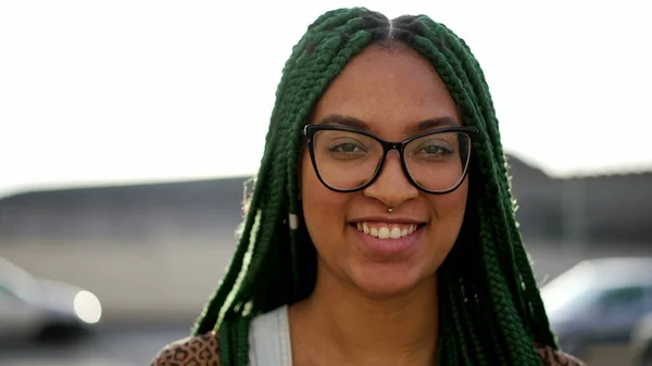 One happy young hispanic black woman standing outdoors smiling. Closeup face portrait of a joyful South American female person with braided hairstyle
