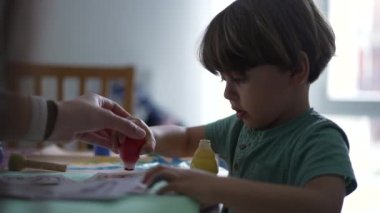 Evde boya yapmak için boya fırçası kullanan küçük bir çocuk. Evde çocuk yaratıcılığı sanatsal aktivitesi. Çocuk boyama