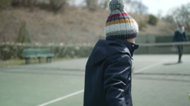 Çocuk tenis raketiyle topa vuruyor kış mevsiminde kışlık kıyafetler giyiyor. Çocuk spor yapıyor.